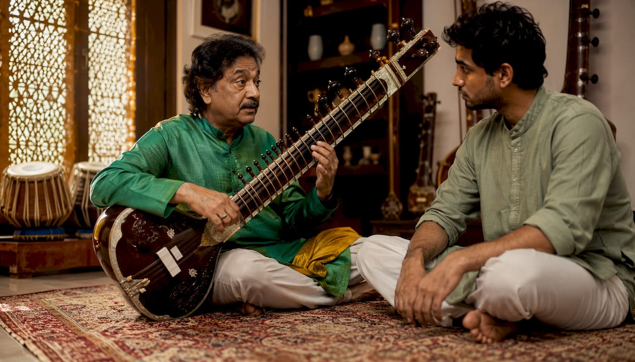 Guru teaching sitar to student in music room