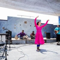 Rajib Karmakar with Dhara World music Joshua Tree Music Festival Rajib Karmakar with Dhara World Music and a woman in a pink dress dancing on a stage with musicians Joshua Tree Music Festival California